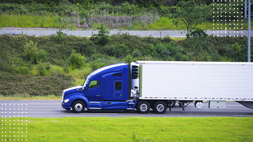 Blue cab semi truck with white trailer driving down road with green grass